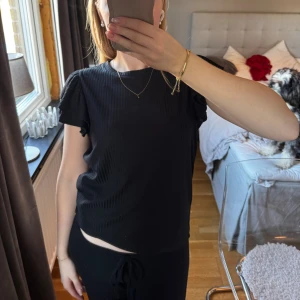 T-shirt med volanger - Säljer en svart T-shirt/topp med söta volanger över axlarna. Toppen är i stolek XS och är i mycket bra skick. Den är köpt på Gekås och var med i Pernilla Wahlgrens kollektion. Hör gärna av dig vid frågor❤️