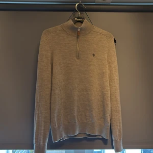 Beige merinoulltröja Morris half zip XS - Snygg beige tröja från Morris i 100% merinoull med half zip och hög krage. Broderad logga på bröstet och ribbade muddar. Perfekt för lager-på-lager och stilren look.