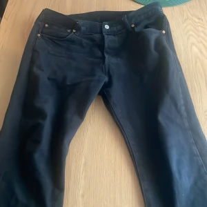 Svarta Levi's 501 jeans 36/32 - Klassiska svarta Levi's 501 jeans med raka ben och fem fickor. Jeansen har knappgylf och den ikoniska läderpatchen bak i midjan. Perfekta för dig som gillar en tidlös och clean look.