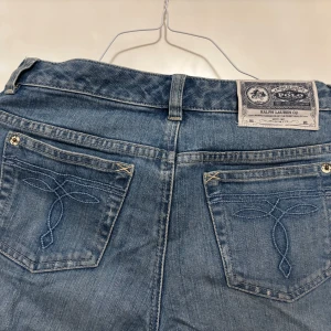Blå jeans från Polo Ralph Lauren - Snygga blå jeans från Polo Ralph Lauren med klassisk femficksdesign och broderade detaljer på bakfickorna. Jeansen har normal passform och är tillverkade i 99% bomull och 1% elastan för lite stretch. Perfekta för en avslappnad och stilren look.