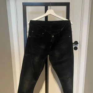 Svarta jeans Tiger of Sweden Sharp 34/32 - Svarta jeans från Tiger of Sweden i modellen Sharp. Snygg tvätt med lätt slitning och klassisk femficksdesign. Jeansen har en rak passform och är tillverkade i ett mjukt bomullsmaterial med stretch för extra komfort.