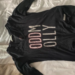 Svart långärmad tröja Odd Molly - Svart långärmad tröja från Odd Molly med tryck framtill och coolt kompassmotiv på ryggen. Tröjan har v-ringning och är gjord i mjuk bomull. Snygga detaljer i vitt och rött på trycket, perfekt för dig som gillar unika prints.