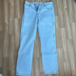 Wrangler ljusblå raka jeans - Ljusblå jeans från Wrangler med klassisk femficksdesign och raka ben. Jeansen har tydliga kontrastsömmar, bälteshällor och läderpatch med logga bak. Tillverkade i bomullsdenim för en tidlös look.