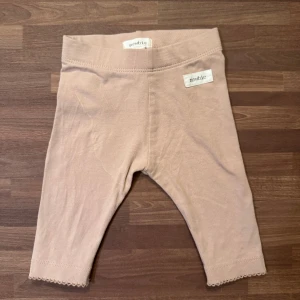 Leggings med rosett - Supersöta dusty pink leggings från Newbie i storlek 56 (1-2 mån). Gullig rosettdetalj bak och små dekorativa kanter vid bensluten. Använda endast en gång, men har en dov fläck som går över ena låret, se bild 1. Inte testat fläckbehandla.