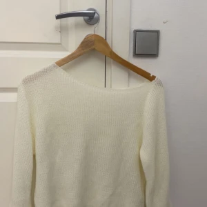 Vit stickad tröja med lång ärm - En enkel och stilren vit stickad tröja med lång ärm med en sne huvud from. Perfekt att slänga på sig när det är lite kyligare ute. Tröjan har en mjuk och luftig känsla och passar till det mesta i garderoben.