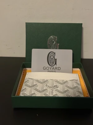 Vit Goy4ard plånbok med mönster - Vit goy4ard plånbok med elegant mönster i snyggt texturerat material. Rymlig och praktisk med flera fack för kort, sedlar och mynt. Stilren och trendig design som passar både vardag och fest. Plånboken är i gott skick och ett perfekt tillbehör för dig som vill kombinera funktion med mode