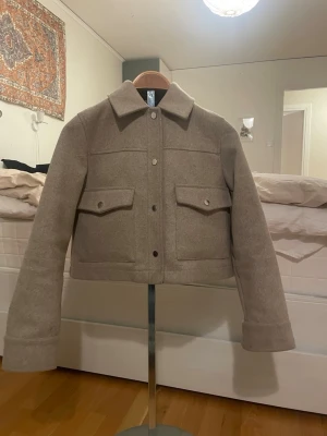 Kappa med fickor - Snygg beige jacka med krage och stora fickor med lock och knappar. Jackan har en croppad passform och stängs med knappar framtill. Perfekt att slänga över en t-shirt för en chill look💕