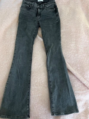 Grå bootcut jeans från Gina Tricot - Snygga grå jeans från Gina Tricot med bootcut passform och klassisk femficksdesign. Jeansen har hög midja och är tillverkade i mjukt bomullsmaterial med en lätt tvättad look. Perfekta för en trendig och avslappnad stil. De är i längden tall