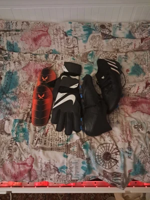 Fotboll skor, handskar,  benskydd och hoodie - Säljer ett par svarta fotbollsskor från Adidas med vita detaljer och blå dobbar. Skorna har en modern design och är tillverkade i syntetmaterial för bra grepp och komfort på planen. Perfekta för dig som vill ta ditt spel till nästa nivå. Ett par nike handskar men bra grepp och ben skydd