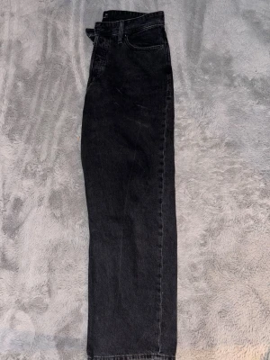 Svarta raka jeans från Jack and Jones  - Klassiska svarta Jack and Jones  jeans med rak passform och femficksmodell. Jeansen har hög midja och är tillverkade i robust denim av bomull. Perfekta för en avslappnad och tidlös stil.