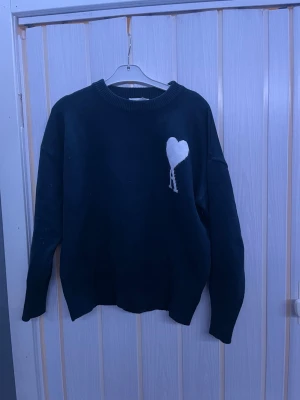 Mörk blå stickad tröja från Ami Paris - Säljer en mörk blå stickad tröja från Ami Paris med deras ikoniska hjärta och A broderat i vitt på bröstet. Tröjan har rund hals, ribbade muddar och lång ärm. Perfekt för dig som gillar stilrena detaljer och vill ha något som sticker ut lite extra. Pris kan diskuteras🤗