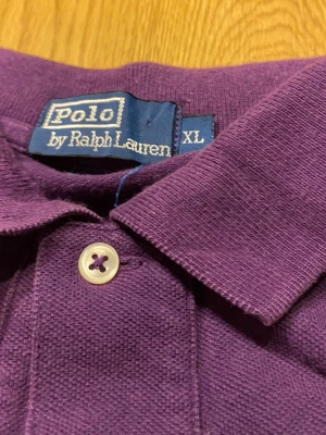 Lila pikétröja från Polo Ralph Lauren XL - Säljer en lila pikétröja från Polo Ralph Lauren i storlek XL. Klassisk pikékrage med knappar framtill och lång ärm. Tröjan är i mjuk bomull och har en clean look utan mönster eller tryck. Perfekt för dig som gillar stilrena plagg med en färgklick.