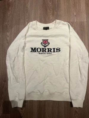 Vit sweatshirt från Morris - Säljer denna fina sweatshirt i färgen vit från Morris med rund halsringning och broderad logga samt Union Jack-detalj på bröstet. Tröjan har ribbade muddar vid ärmslut och nederkant. Perfekt för en avslappnad och stilren look. Tröjan är i storlek S men passar M perfekt! 