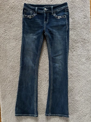 Grace in LA , Mörkblå bootcut jeans med broderi - Grace in LA jeans, Snygga mörkblå bootcut jeans med kontrastsömmar och broderade detaljer vid fickorna. Jeansen har klassisk femficksdesign och en lätt utsvängd passform nertill. Perfekta för dig som vill ha en cool och avslappnad stil.