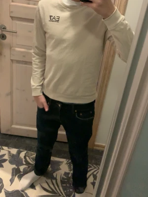 Beige sweatshirt från EA7 Emporio Armani - Snygg beige sweatshirt från EA7 Emporio Armani och inte en ända skada med rund halsringning och diskret logga på bröstet. Tröjan har en klassisk passform med ribbade muddar vid ärmslut och nederkant. Perfekt för en stilren och avslappnad look.