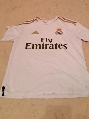 Real Madrid 2019/2020 tröja - Hallå!  Jag säljer en Real Madrid t-shirt i mycket bra skick. Den är väl omhändertagen och ser nästan ny ut. Perfekt för dig som vill visa ditt stöd för laget med stil.  Priset är 300 kr, vilket jag tycker är ett bra pris med tanke på skicket och att det är en officiell Real Madrid t-shirt. Jag är öppen för snabba affärer!  Tveka inte att höra av dig om du är intresserad eller har några frågor. Först till kvarn gäller!