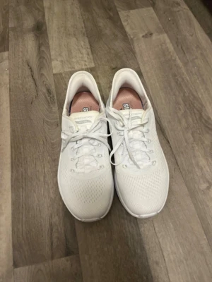 Vita sneakers från Skechers - Stilrena vita sneakers från Skechers med mesh-ovandel och klassisk snörning. Skorna har en rund tå och platt sula för skön komfort. Perfekta för dig som gillar en enkel och sportig look. Diskret Skechers-logga på sidan.