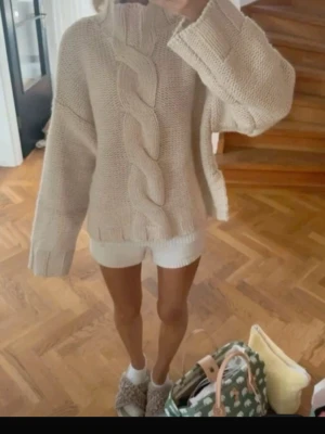 Beige chunky stickad tröja - Säljer en beige chunky stickad tröja med stor fläta framtill och höga muddar. Tröjan har oversized passform, hög hals och långa ärmar. Perfekt för dig som gillar en mysig och trendig look.