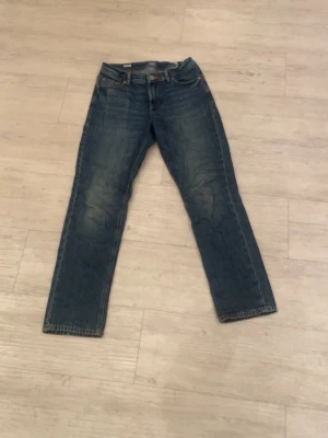 Jack & Jones blå jeans straight fit - Klassiska blå Jack & Jones  jeans med rak passform och fem fickor. Jeansen har en tidlös look med knappgylf och den ikoniska läderlappen bak i midjan. Perfekta för dig som gillar en avslappnad och autentisk denimstil.