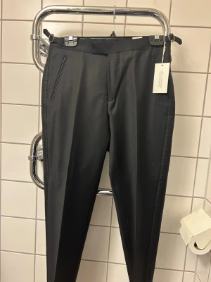 Svarta kostymbyxor från VOLT - Snygga svarta kostymbyxor från VOLT med raka ben och diskreta fickor fram och bak. Byxorna har en klassisk midja och är tillverkade i ett slätt material som ger en stilren look. Perfekta för dig som vill ha en clean och modern stil. Helt nya, oanvända med lapp kvar. Nypris 999kr.