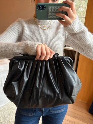 Svart handväska i skinnimitation - Säljer en svart handväska med axelrem i skinnimitation. Man kan välja att bära den som en clutch genom att stoppa in snöret i väskan eller bära den på axeln🥰