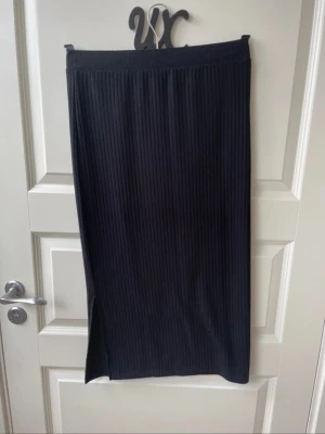 Svart ribbad kjol från PIECES i strl S - Snygg svart långkjol från PIECES med ribbad struktur och slits på sidan. Kjolen har en enkel och stilren design som passar till många olika looks. Perfekt för dig som gillar minimalistisk stil.