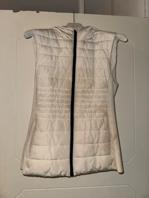Vit dunväst  - Vit väst från Zara, passar som sportväst men även till vardags till en tight ute outfits. Perfekt att slänga över en hoodie för extra värme. Enkel och stilren design som passar till det mesta.  Behövs en ordentlig tvätt eller rengöring med våtservetter. Annars i fint skick, inga skador. Jag kan rengöra den till er och skicka bild innan ni köper om ni är osäkra! 