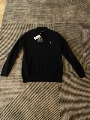 Svart half zip tröja från Polo Ralph Lauren - Säljer en svart långärmad tröja från Polo Ralph Lauren med klassisk vit logga på bröstet och half zip-dragkedja. Tröjan har en stilren, normal passform och är tillverkad i mjuk ull som passar perfekt till höst och vinter. Obs storlek står L men sitter som M då den är lite mer slim fit!!! Helt ny half zip från Ralph lauren som passar till allt och alla och kan aldrig gå fel endast testad 1 gång hör av er vid frågor och funderingar!😁