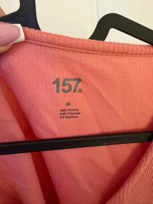 Rosa croppad topp från 157 - Säljer en ljusrosa croppad topp från 157 med ribbad struktur. Toppen har lång ärm, v-ringning och en knapp framtill. Materialet är en mix av viskos, polyester och elastan vilket gör den mjuk och stretchig. Perfekt till jeans eller kjol!