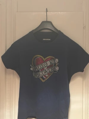 Mörkblå t-shirt Zadig & Voltaire hjärta - Cool mörkblå t-shirt från Zadig & Voltaire med ett stort hjärta i rött, gult och silver på bröstet. T-shirten har korta ärmar och rund hals. Perfekt för dig som gillar statement-plagg med snygga detaljer.