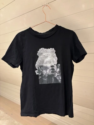 Svart t-shirt - Cool svart t-shirt med ett unikt konstnärligt tryck på bröstet. T-shirten har rund hals och korta ärmar. Perfekt för dig som gillar streetwear och statement-plagg.