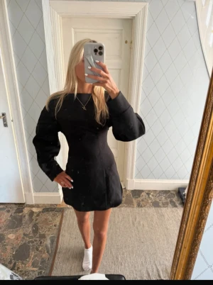 Svart kort klänning med öppen rygg - Svart kort klänning från (aldrig använd)PrettyLittleThing med puffiga långärmar, markerad midja och cool öppen rygg med . Klänningen har en slits i nederkanten (använder första säljarens bilder)