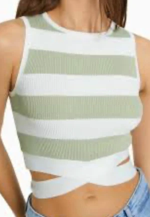 Randig ribbad linnetopp med knyt - Säljer en ribbad linnetopp från Bershka  med breda olivgröna och vita ränder. Toppen är ärmlös och croppad. Perfekt för dig som gillar en chill och trendig stil.Nedtill har den breda vita band som korsas i midjan eller på ryggen