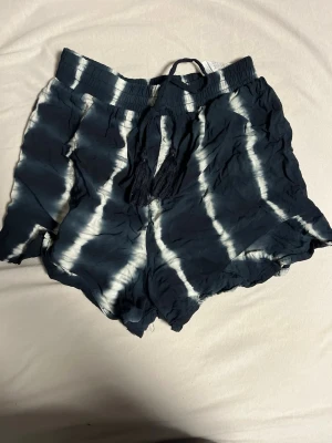 Svarta shorts med batikmönster och snörning - Snygga svarta shorts med vitt batikmönster och elastisk midja med snörning. Lätta och luftiga, perfekta för sommaren. Avslappnad passform och mjukt material som känns skönt mot huden.