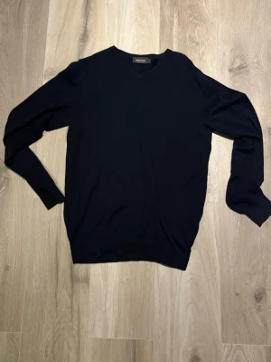 Svart v-ringad tröja Dressmann - Klassisk svart tröja från Dressmann i mjuk bomull. V-ringad modell med långa ärmar och ribbade muddar vid ärmslut och nederkant. Perfekt basplagg för en clean och enkel stil.