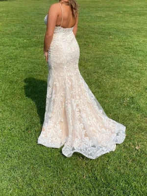 Balklänning/Bröllopsklänning - Champagnefärgad spetsklänning.                 Elegant långklänning i champagnefärg med tunna axelband och vacker vit spets över hela klänningen. Klänningen har figurnära passform upptill och en utsvängd kjol med släp. Perfekt för bal, student och brudklänning. Klänningen är från Morilee by Madeline Gardenr. Använd 1 gång och därefter kemtvättad. Passar 36/38. Kan tänkas gå ner lite i pris vid snabb affär.