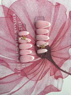 Rosa press-on naglar med pärldekor - Snygga press-on naglar i ljusrosa med vit fransk tipp. Några naglar har dekorationer med små pärlor och guldfärgade detaljer. Formen är almond och materialet är plastl gel. Perfekt för dig som vill ha en söt och trendig look.