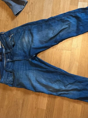 Blå replay jeans  - Snygga blå replay  jeans med klassisk fyrficksdesign och stretchigt material som sitter tajt längs benen. Jeansen har en något tvättad look med ljusare partier och smala ben, perfekta till en avslappnad stil. Liten defekt vi gylfen dock ser man den inte och passar in bra i modellen 