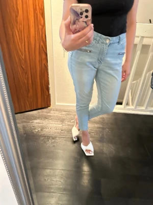 Ljusblå högmidja jeans  - Ljusa jeans med dragkedjedetaljer framtill. I använd skick, en ficka är trasig se bild. De upplevs som 36 i storlek. Jag är 160 cm lång