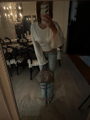 Vit topp med vida ärmar - Trendig vit topp med vida, långa ärmar och rund halsringning. Perfekt för dig som gillar en avslappnad men ändå stilren look. Toppen har en enkel design utan mönster och är lätt att matcha med jeans eller kjol.