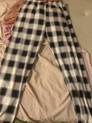 Rutiga pyjamasbyxor i svart och vitt - Snygga pyjamasbyxor med svart och vitt rutmönster. Byxorna har resår i midjan och raka ben, perfekta för mysiga hemmakvällar. Tillverkade i mjukt tyg som känns skönt mot huden.