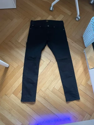 Svarta skinny jeans från Lee - Snygga svarta straight/skinny  jeans från Lee med klassisk femficksdesign och ganska tajt. Jeansen har en enkel look utan slitningar eller dekorationer, perfekta till alla outfits. Tillverkade i mjukt och stretchigt jeanstyg för extra komfort.