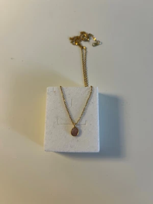 Guldhalsband med rosa sten - Snyggt halsband i guldfärgad metall med en rund, lila amethyst sten som hänge. Kedjan är tunn och har ett klassiskt lås. Gjord av stainless steel. Handgjort i Portugal, perfekt att ge i present.  😊