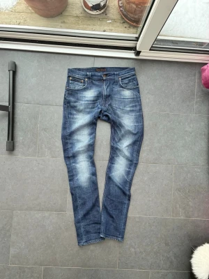 Sjukt feta blåa jeans från Nudie - Säljer ett par blå jeans från Nudie Jeans modell Thin Finn med cool tvättad effekt. Jeansen har normal midja och raka ben med smal passform. Tillverkade i slitstarkt jeanstyg som sitter snyggt och bekvämt.