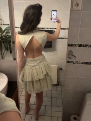 Ljusgrön kort klänning med volanger - Säljer en ljusgrön kort klänning med volangkjol och öppen rygg. Klänningen har ett brett midjeband med en dekorativ ringdetalj framtill och är ärmlös. Perfekt för dig som gillar unika detaljer och en feminin look. Storlek m men passar även s