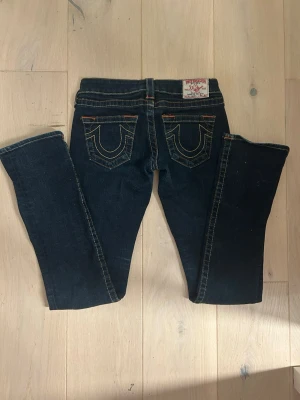 Mörkblå True Religion jeans - Snygga mörkblå jeans från True Religion med klassiska kontrastsömmar och ikoniska fickdetaljer bak. Modellen har låg midja och raka ben. Perfekta för dig som gillar en tidlös och cool look.