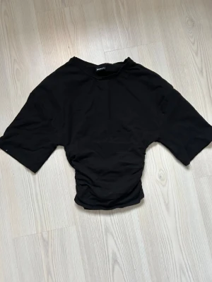 Svart croppad topp från Gina Tricot - Säljer en svart croppad topp från Gina Tricot med korta ärmar och rund hals. Toppen har en enkel och clean design i mjukt bomullsmaterial, perfekt till jeans eller kjol. Passformen är normal och toppen är lätt att styla till olika looks.