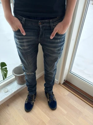 Mörkblå skinny jeans med slitningar. - Snygga mörkblå skinny jeans med slitningar och lätt tvättade detaljer. Jeansen har klassisk femficksdesign, låg midja och smal passform. Perfekta för en trendig och avslappnad look.