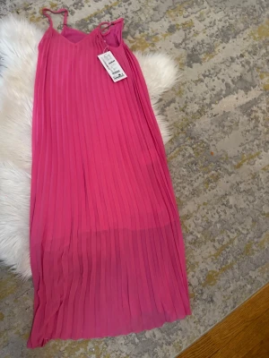 Plisserad rosa långklänning Amisu - Säljer en plisserad rosa långklänning från Amisu med tunna axelband och v-ringad hals. Klänningen har ett luftigt fall och är perfekt för sommarens alla tillfällen. Materialet är lätt och känns bekvämt mot huden.