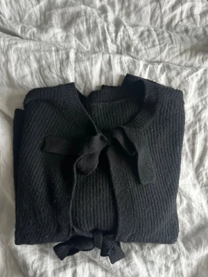 Svart ribbad kofta med knytband, L/XL - Väldigt fin stickad tröja! Inköpt från Nelly. Mycket fin kvalitet och i mycket bra skick! Använd fåtal gånger. Storlek L/XL.